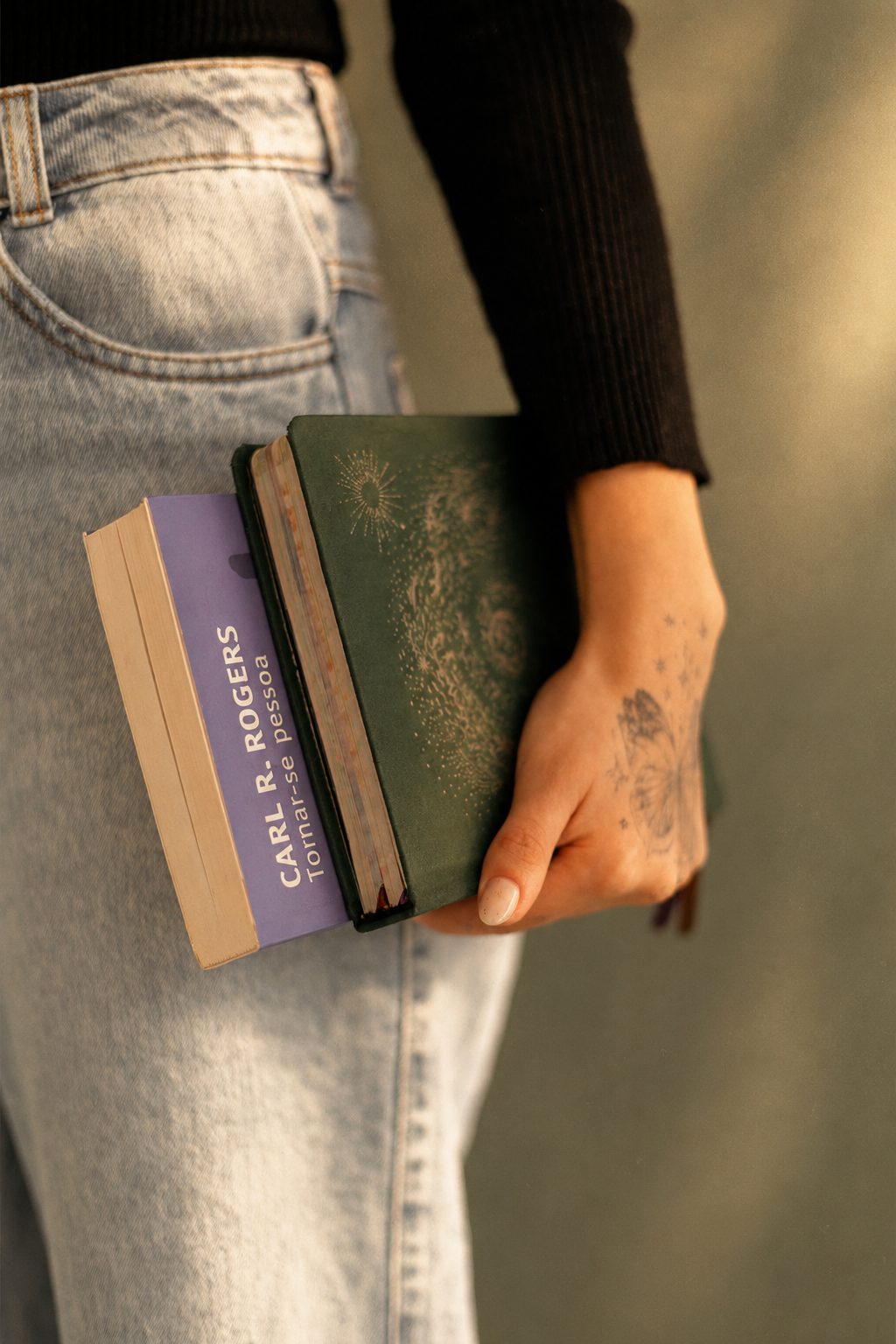 Detalhe da mão de Rapha segurando dois livros, incluindo Tornar-se pessoa, de Carl R. Rogers